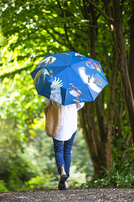 a woman walking down a road holding a blue umbrella