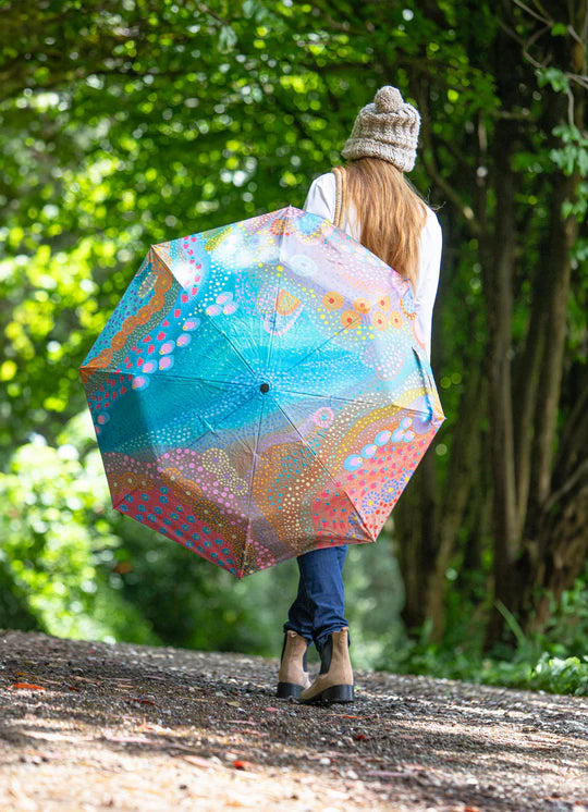 a woman walking down a dirt road holding an umbrella